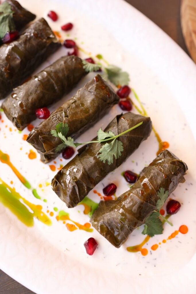 Savory stuffed grape leaves on a plate with vibrant pomegranate seeds.